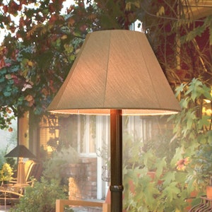 May include: A brown outdoor floor lamp with a beige fabric shade. The lamp is on a patio with chairs and plants.