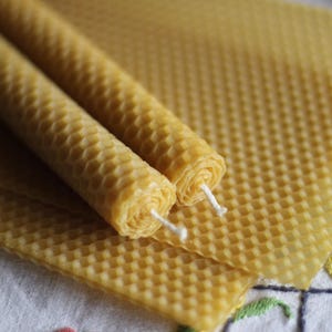 Puede incluir: Dos velas de cera de abeja en forma de panal con mechas blancas. Las velas están sobre una lámina de cera de abeja en forma de panal.