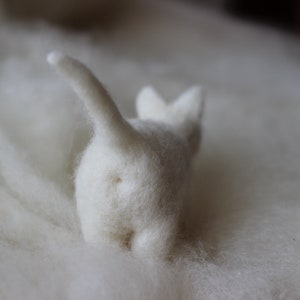 Peut inclure: Une figurine de chat en feutre blanc avec une queue moelleuse, posée sur une surface moelleuse blanche.