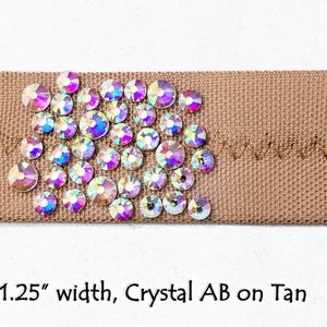 May include: A 1.25 inch wide tan ribbon with crystal AB rhinestones. The rhinestones are arranged in a cluster and have a rainbow iridescent effect.