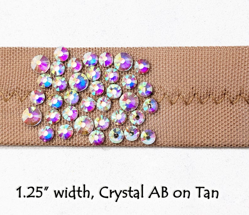 May include: A 1.25 inch wide tan ribbon with crystal AB rhinestones. The rhinestones are arranged in a cluster and have a rainbow iridescent effect.