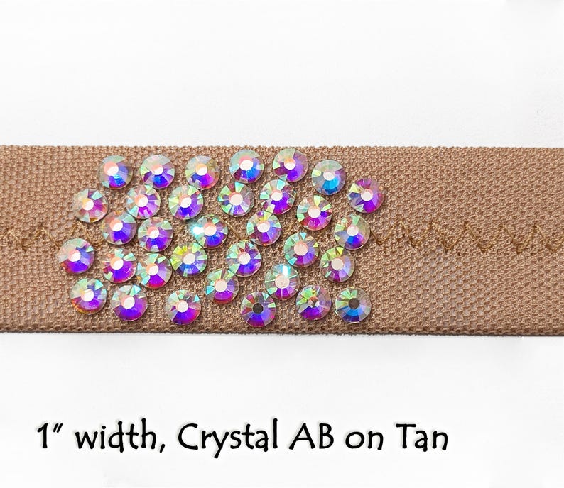 May include: A close-up of a 1 inch wide tan ribbon with crystal AB rhinestones. The rhinestones are arranged in a cluster and have a rainbow iridescent effect.