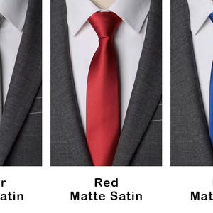 K&ouml;nnte beinhalten: Drei Krawatten in Silber, Rot und Blau, jeweils mit matter Satin-Oberfl&auml;che. Die Krawatten sind gebunden und werden &uuml;ber einem wei&szlig;en Hemd mit Kragen und einem dunkelgrauen Sakko getragen. Text unter jeder Krawatte benennt die Farbe.