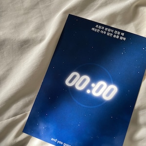 Könnte beinhalten: Ein blau-weißer Druck mit dem Text "00:00" in einer großen, leuchtenden Schriftart. Der Druck enthält auch den Satz "and you gonna be happy" am unteren Rand. Der Hintergrund ist ein Blauton mit Sterneneffekt.