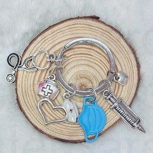 May include: Silver keychain with a variety of charms, including a stethoscope, a heart, a syringe, a face mask, and a small red cross. The charms are attached to a silver ring.