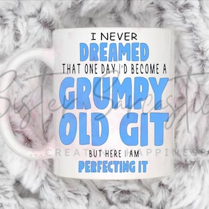 Può includere: Tazza in ceramica bianca con la scritta "I NEVER DREAMED THAT ONE DAY I'D BECOME A GRUMPY OLD GIT BUT HERE I AM PERFECTING IT" in blu e nero. La tazza ha un manico bianco ed è appoggiata su uno sfondo bianco e soffice.