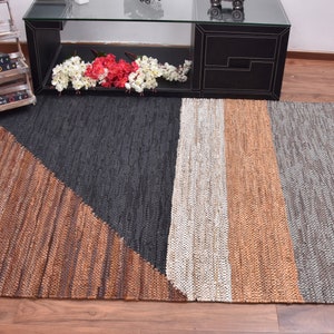 May include: A rectangular woven rug with a geometric design. The rug is made of natural fibers and has a brown, black, white, and gray color scheme.