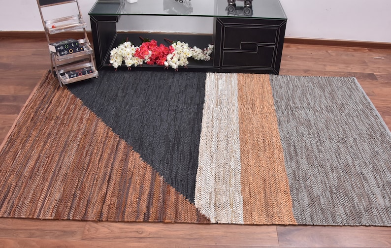May include: A rectangular woven rug with a geometric design. The rug is made of natural fibers and has a brown, black, white, and gray color scheme.