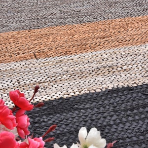 May include: A close-up of a multi-colored woven rug with a black, white, brown, and orange pattern. The rug is made of small, round pieces of material that are woven together. The rug is in focus, and the background is blurred.