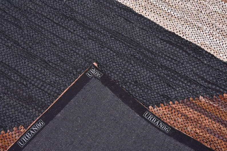 May include: Close-up of the back of a black, brown, and white leather rug with the text "URBAN86" printed on the edge.