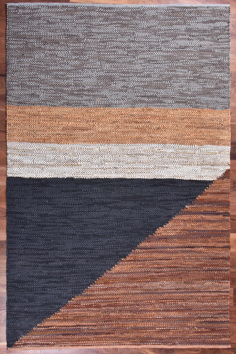 May include: A woven rug with a geometric design in shades of gray, brown, and beige. The rug has a textured surface and a modern, minimalist style.