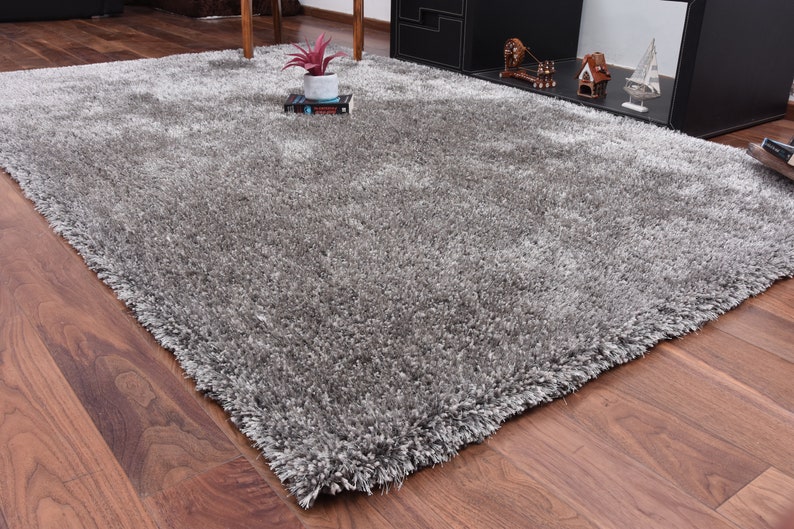 K&ouml;nnte beinhalten: Ein flauschiger, grauer Shaggy-Teppich mit weicher, flauschiger Textur. Der Teppich liegt auf einem Holzboden.
