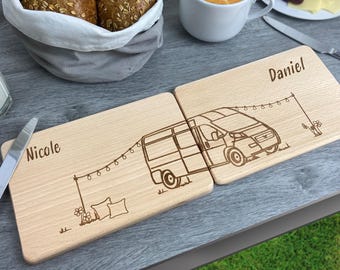 May include: Two rectangular light-colored wooden cutting boards placed side-by-side. The boards feature a laser-engraved design of a camper van with string lights, flowers, and pillows. The name Nicole is engraved on the left, and Daniel on the right.