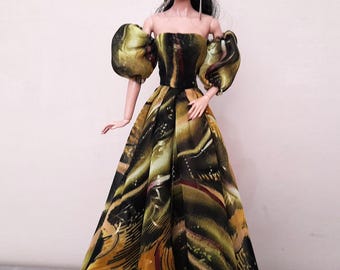 May include: A fashion doll wearing a strapless gown with a flowing skirt. The dress features a pattern of olive green, black, and gold abstract shapes. The doll has black hair and is wearing long silver earrings.