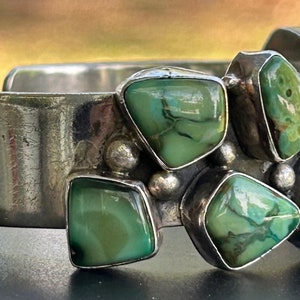 May include: A silver cuff bracelet with a cluster of green turquoise stones set in the metal. The stones are irregularly shaped and have a mottled pattern.