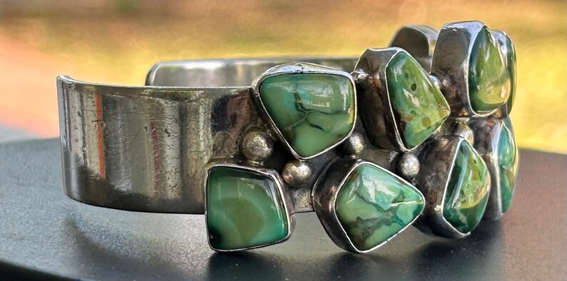May include: A silver cuff bracelet with a cluster of green turquoise stones set in the metal. The stones are irregularly shaped and have a mottled pattern.