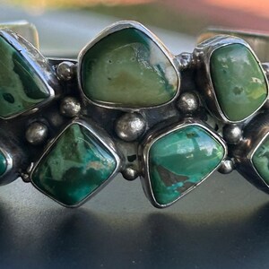 May include: A silver bracelet with multiple green turquoise stones set in a geometric pattern.