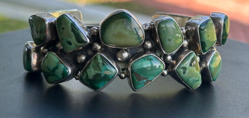 May include: A silver bracelet with multiple green turquoise stones set in a geometric pattern.