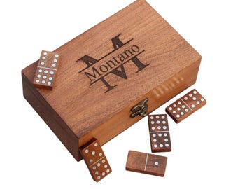 Könnte beinhalten: Ein Domino-Set aus Holz mit passender Box. Die Box ist mit dem Namen "Montano" und der römischen Zahl "VI" graviert. Die Dominosteine sind braun mit weißen Punkten. Die Box hat einen Metallverschluss.