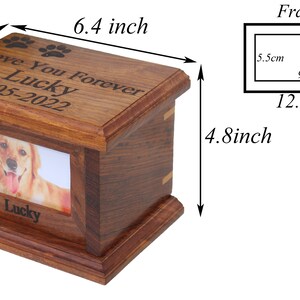 K&ouml;nnte beinhalten: Eine h&ouml;lzerne Tierurne mit einem Bilderrahmen, graviert mit dem Text "Love You Forever Lucky 2005-2022". Die Urne ist 16,3 cm lang, 13,7 cm breit und 12,2 cm hoch.