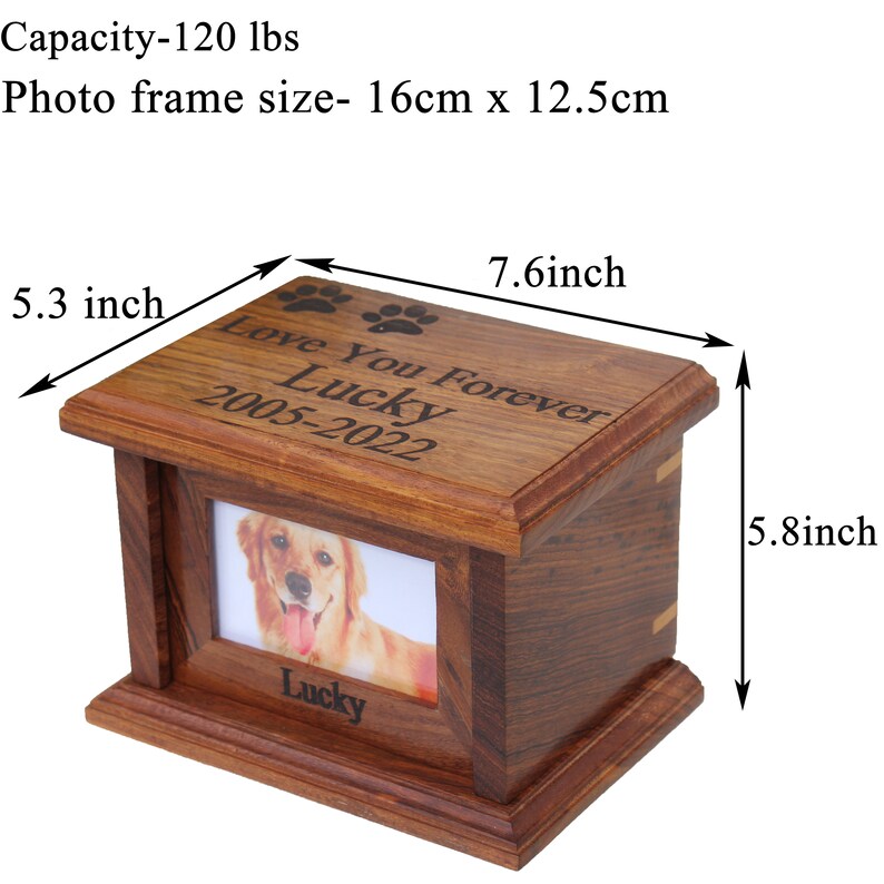 K&ouml;nnte beinhalten: Eine h&ouml;lzerne Tierurne mit einem Bilderrahmen, graviert mit "Love You Forever Lucky 2005-2022". Die Urne ist 19,3 cm breit, 14,7 cm hoch und 13,5 cm tief.