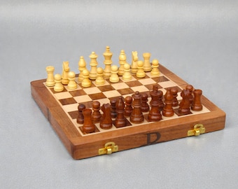 Könnte beinhalten: Ein hölzernes Schachspiel mit Schachbrett und Schachfiguren. Das Schachbrett ist braun und beige mit einem karierten Muster. Die Schachfiguren sind hell- und dunkelbraun. Das Set steht auf einer grauen Oberfläche.