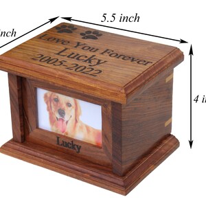 K&ouml;nnte beinhalten: Eine h&ouml;lzerne Tierurne mit einem Bilderrahmen und einer eingravierten Inschrift "Love You Forever Lucky 2005-2022". Die Urne ist 14 cm lang und 10 cm breit.