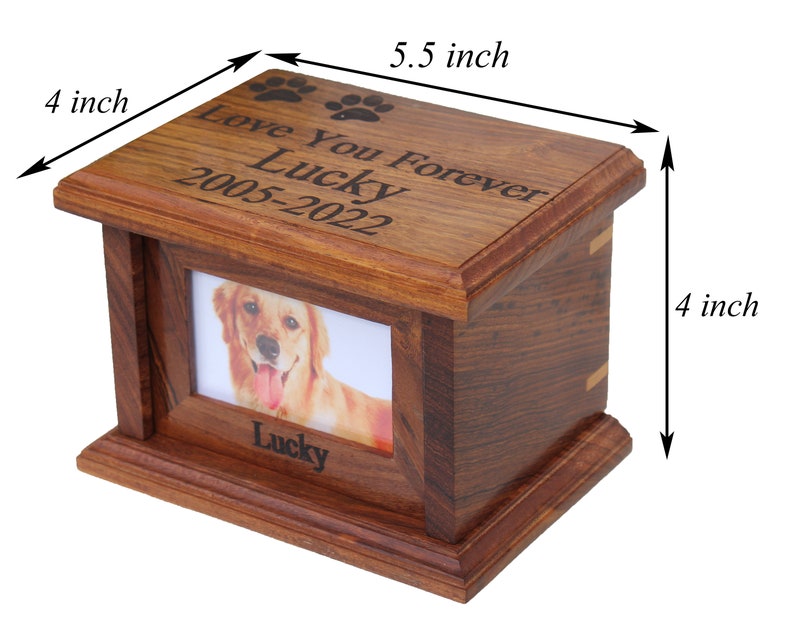 K&ouml;nnte beinhalten: Eine h&ouml;lzerne Tierurne mit einem Bilderrahmen und einer eingravierten Inschrift "Love You Forever Lucky 2005-2022". Die Urne ist 14 cm lang und 10 cm breit.