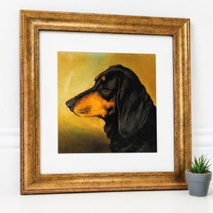 May include: A framed square art print featuring a profile portrait of a black and tan dachshund against a warm, golden-yellow background. The artwork is encased in a wide, ornate, metallic gold frame with a textured finish and a white mat border.