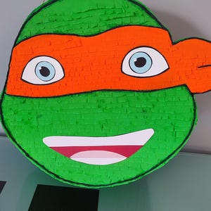 May include: Green and orange Teenage Mutant Ninja Turtles pi&ntilde;ata with a smiling face and a black eye mask.
