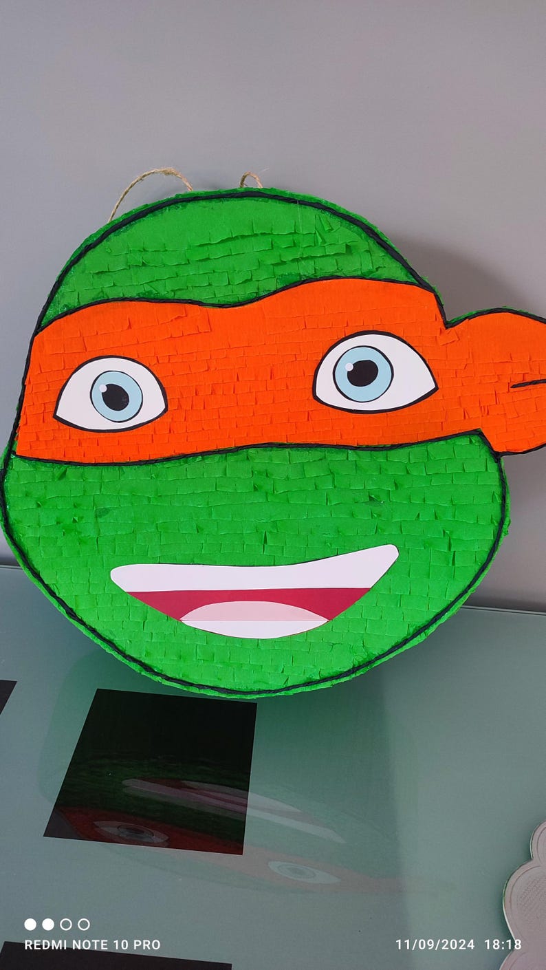 May include: Green and orange Teenage Mutant Ninja Turtles pi&ntilde;ata with a smiling face and a black eye mask.