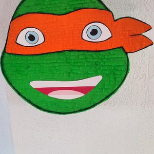 May include: Green and orange Teenage Mutant Ninja Turtles pi&ntilde;ata with a smiling face and blue eyes.