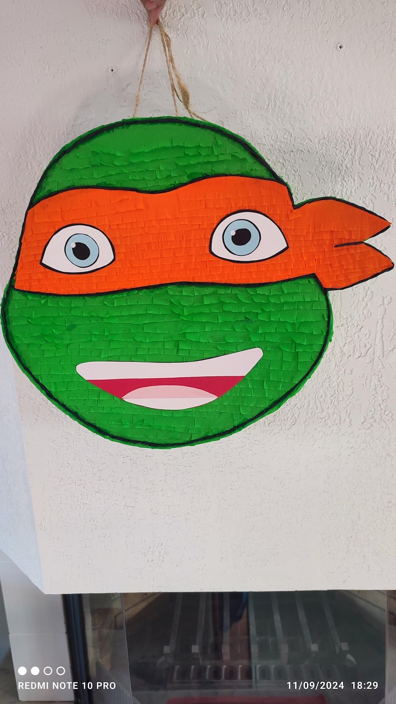 May include: Green and orange Teenage Mutant Ninja Turtles pi&ntilde;ata with a smiling face and blue eyes.