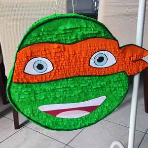 May include: Green and orange Teenage Mutant Ninja Turtles pi&ntilde;ata with a smiling face and a black eye mask.