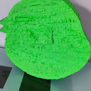 May include: A green pinata shaped like a bird with a string loop on top.