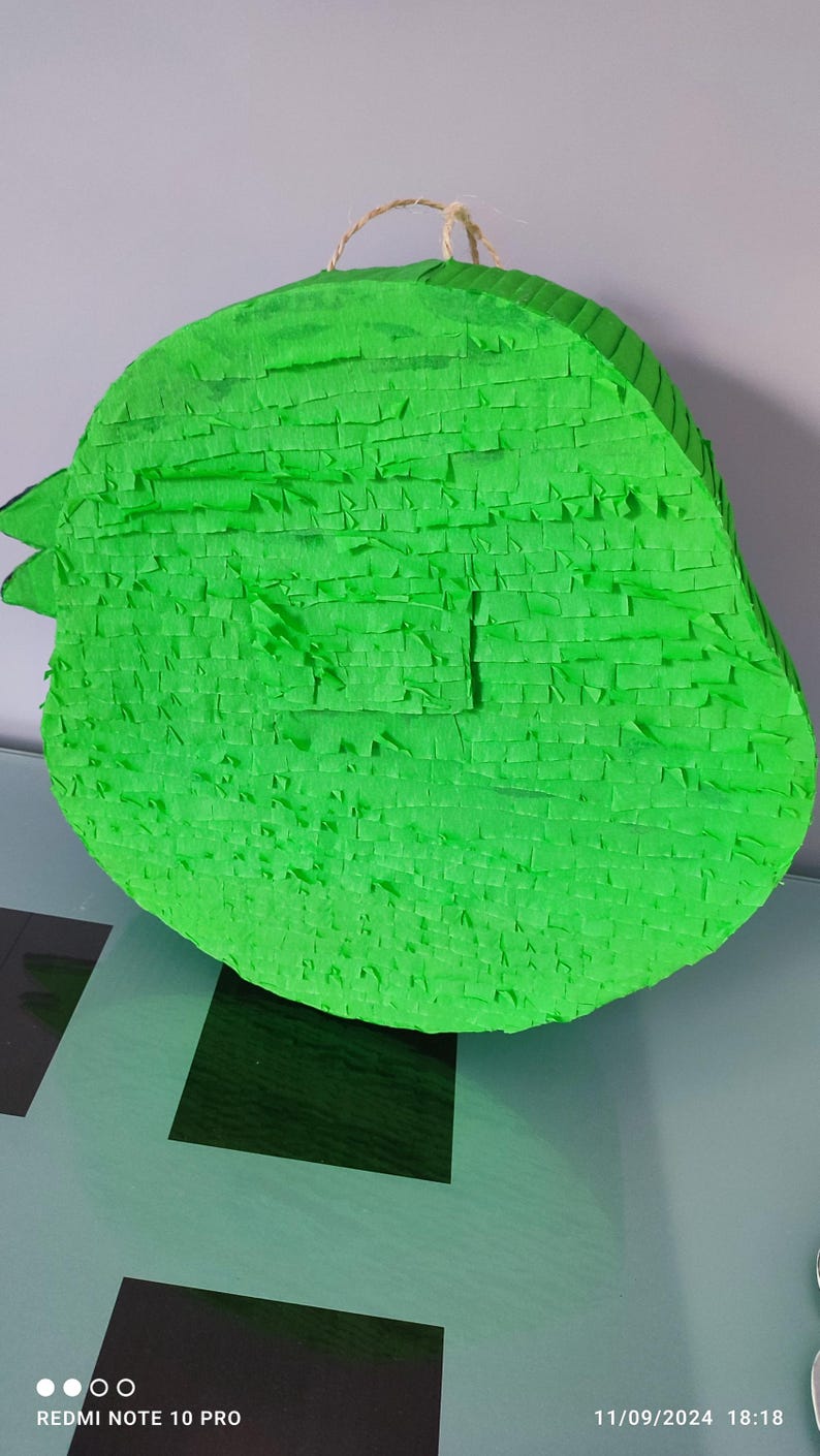 May include: A green pinata shaped like a bird with a string loop on top.