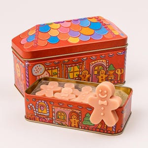 May include: A red, gingerbread house-shaped tin with a colorful roof and gingerbread man illustrations. The open tin reveals several light pink gingerbread man-shaped soaps. A single soap stands upright in the front.
