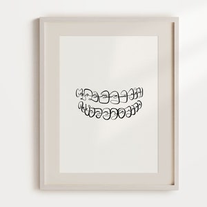 Puede incluir: Un dibujo en blanco y negro de una boca con brackets. El dibujo está enmarcado en un marco blanco y está colgado en una pared blanca.