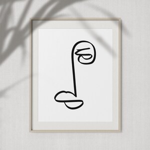 May include: A black and white line drawing of a face with a single eye and a mouth. The drawing is framed in a simple, light brown frame.