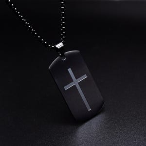 Könnte beinhalten: Eine schwarze Kettenkette mit einem schwarzen Metall-Hundeanhänger mit einem silbernen Kreuz.