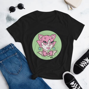 Op de afbeelding: Zwart T-shirt met een groene cirkelvormige afbeelding van een roze kat met blauwe ogen en een roze strik. De tekst "Deb" staat onder de kat.