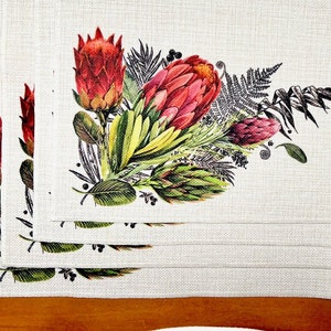 May include: Set of four white linen placemats featuring a floral design with red and green proteas, ferns, and other foliage.