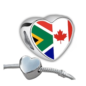 May include: A silver heart-shaped charm with the flags of South Africa and Canada on it. The charm is attached to a silver chain.