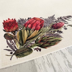 May include: A white fabric placemat featuring a printed design of red and green protea flowers and leaves.