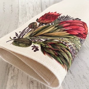 May include: A folded white linen napkin with a printed design of red and green protea flowers.