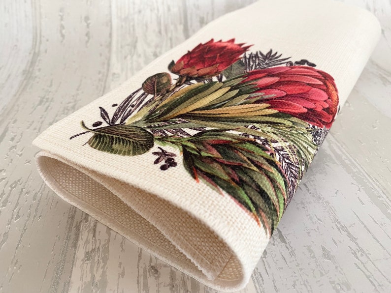 May include: A folded white linen napkin with a printed design of red and green protea flowers.