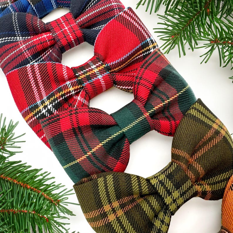 May include: A collection of plaid bow ties in various colors, including red, green, and blue. The bow ties feature classic tartan patterns with contrasting stripes. The image is set against a white background with evergreen sprigs.