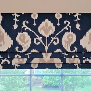 May include: A navy blue roman blind with a white and beige ikat pattern. The blind is mounted on a window with a white frame.