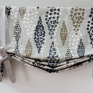 May include: A gray, white, blue, and brown patterned valance with a gathered, pleated design. The valance has two ties on each side that are tied in a bow.