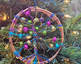 May include: A copper wire tree of life ornament with colorful beads. The ornament is hanging on a Christmas tree.